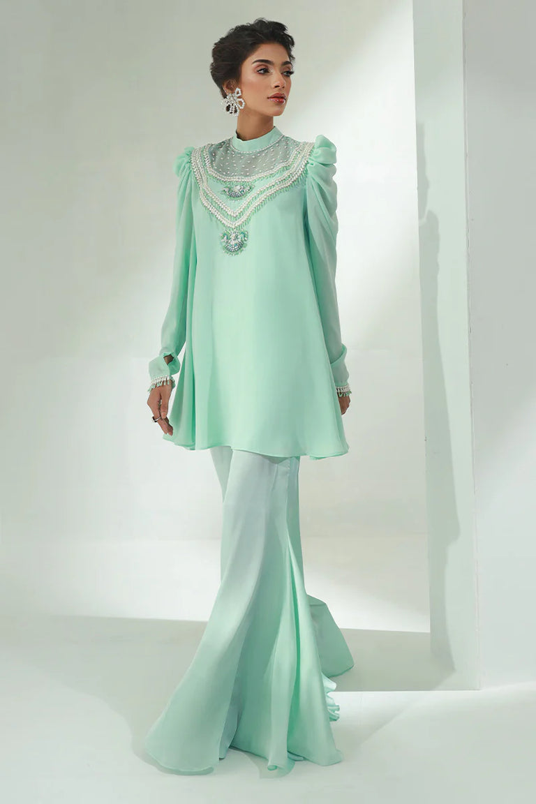 Woman wearing a light green traditional outfit with intricate detailing on a white background