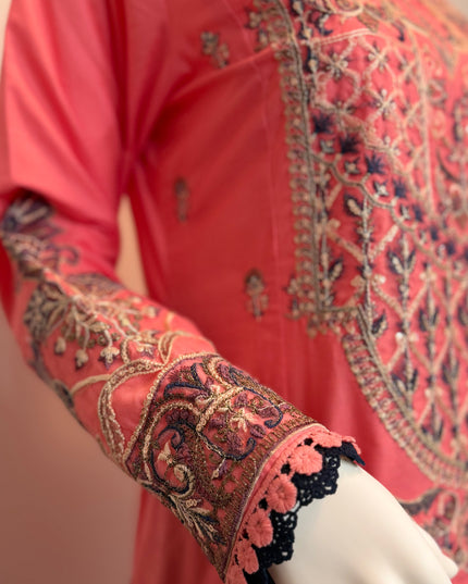 Close-up of a coral pink embroidered garment with intricate patterns on a mannequin.