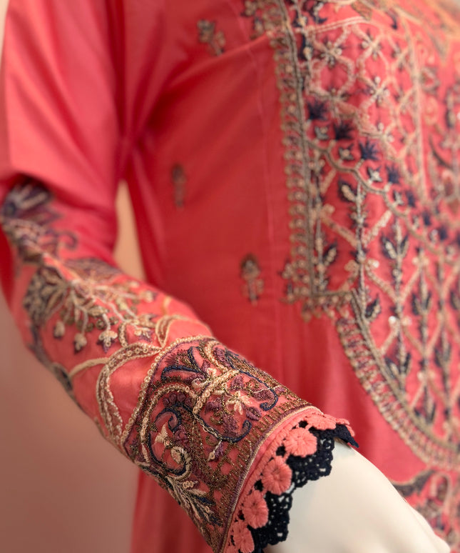 Close-up of a coral pink embroidered garment with intricate patterns on a mannequin.