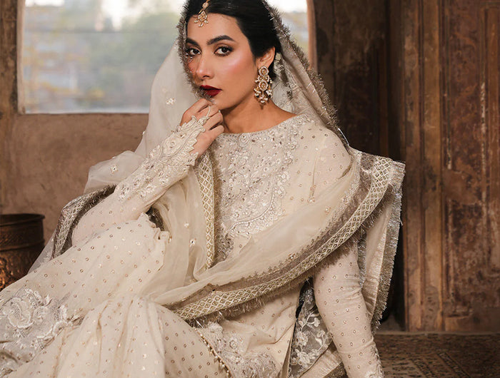 Woman in traditional white embroidered outfit sitting in a decorative interior setting.