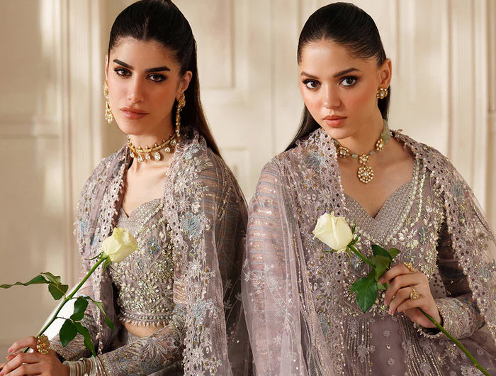 Two women in elegant silver traditional outfits holding white roses against a neutral background.