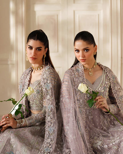 Two women in elegant silver traditional outfits holding white roses against a neutral background.