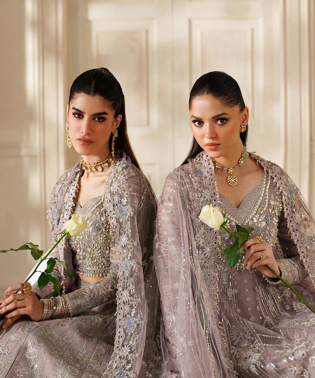 Two women in elegant silver traditional outfits holding white roses against a neutral background.