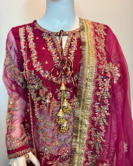 Decorative red garment with gold and multicolor embroidery on a mannequin against a plain background