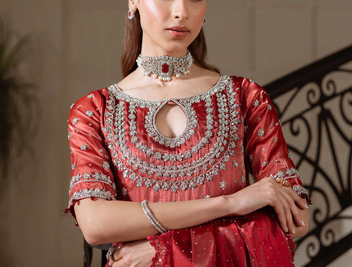 Woman in a red traditional outfit with intricate designs and jewelry indoors.