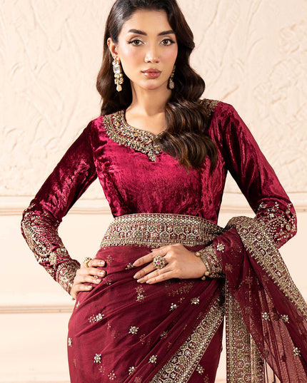 Woman wearing a maroon saree with gold embroidery against a beige background