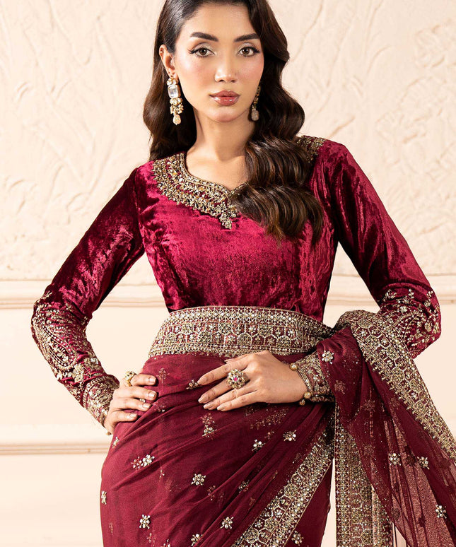 Woman wearing a maroon saree with gold embroidery against a beige background
