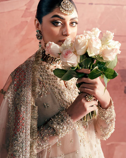 Woman in traditional attire holding flowers against a pink background