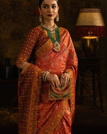 Woman in traditional orange saree with jewelry in a dimly lit room