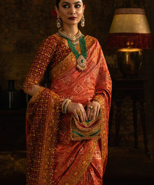 Woman in traditional orange saree with jewelry in a dimly lit room
