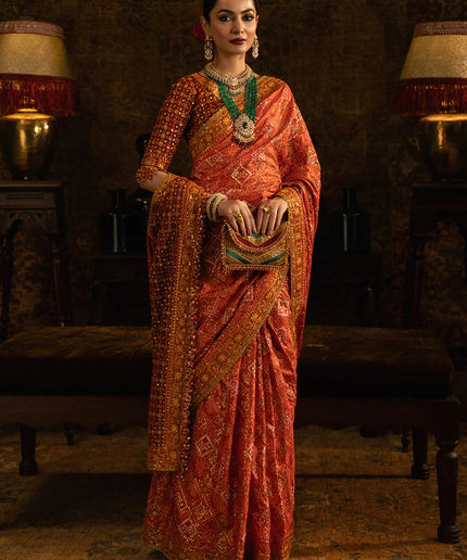 Woman in a traditional orange saree with intricate patterns in a dimly lit room.