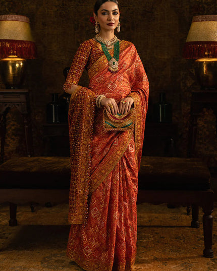 Woman in a traditional orange saree with intricate patterns in a dimly lit room.