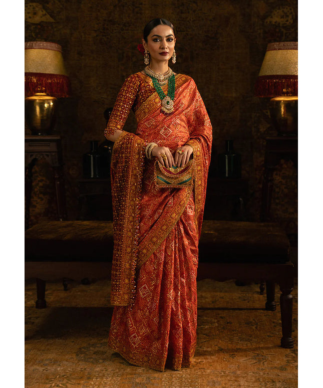 Woman in a traditional orange saree with intricate patterns in a dimly lit room.