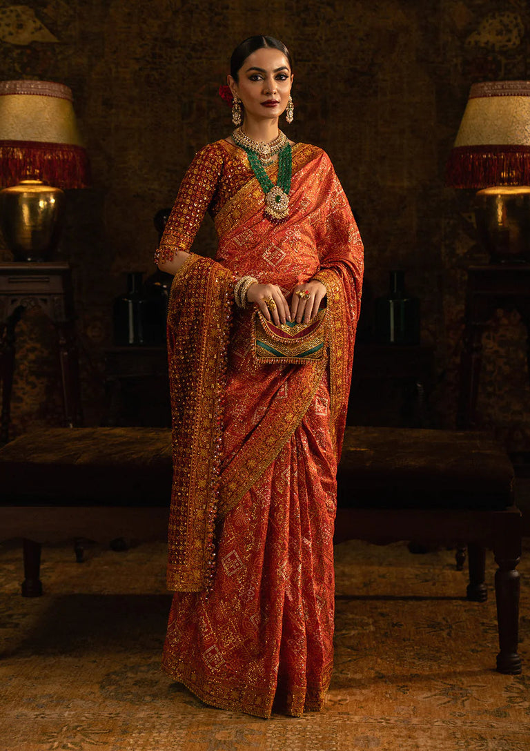Woman in a traditional orange saree with intricate patterns in a dimly lit room.