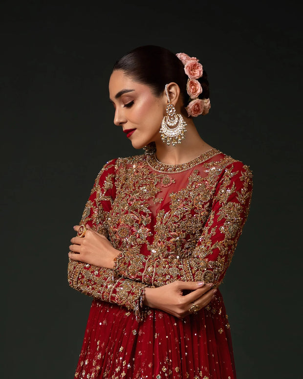 Woman wearing a red and gold embroidered traditional outfit with floral hair accessories on a dark background