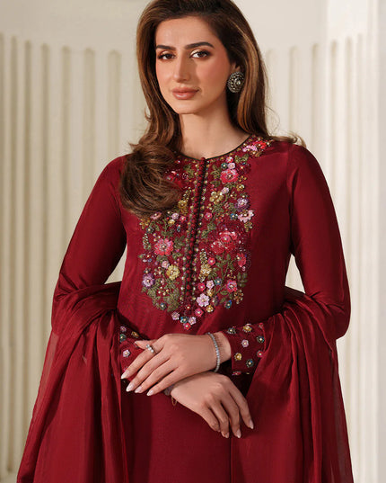 Woman wearing a maroon traditional outfit with floral embroidery in a well-lit room.